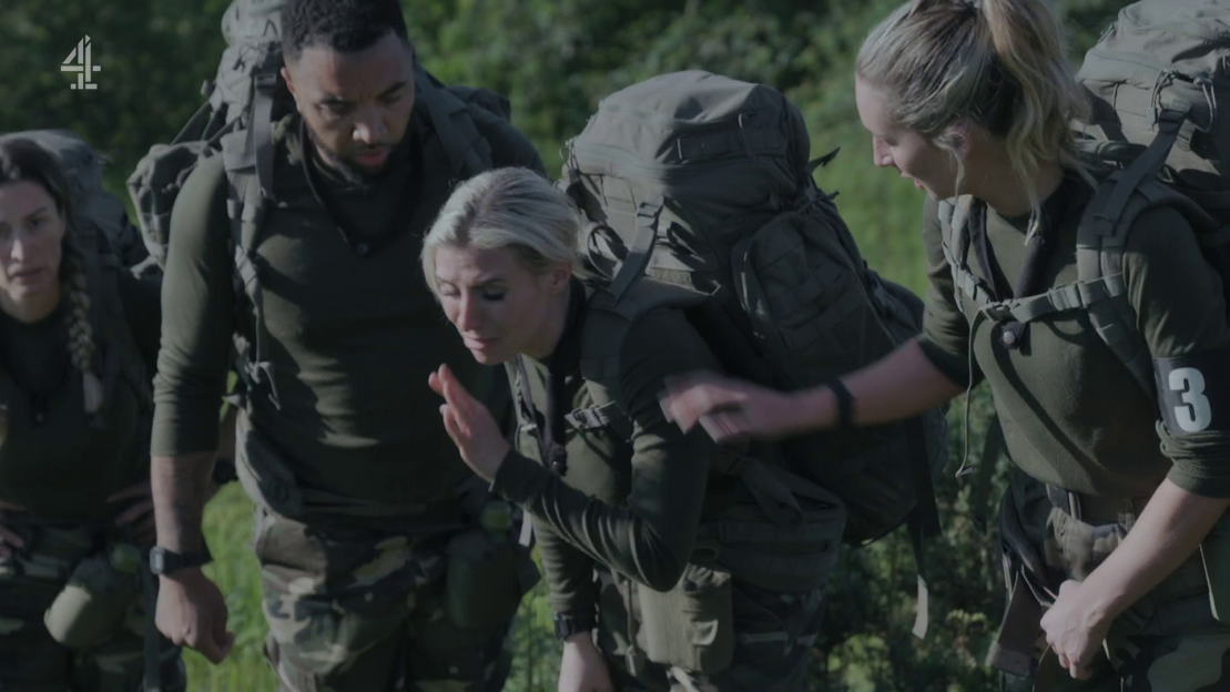 Soldiers carrying heavy backpacks; one woman appears to be struggling.