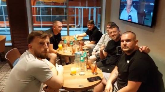 Group of men sitting around tables on a ferry, drinking.