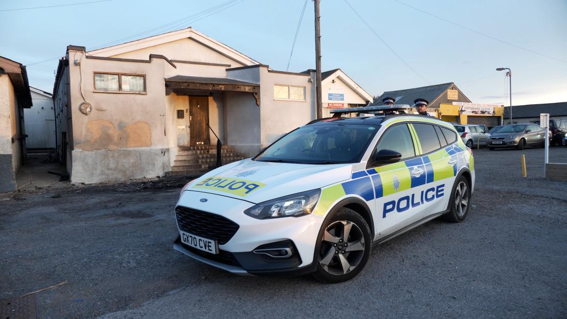 Police car parked in front of a mosque with fire damage to its entrance.