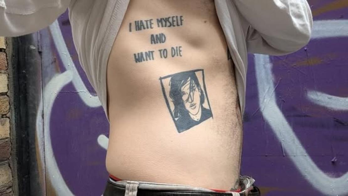 Tattoo on a person's abdomen that says "I hate myself and want to die" above a portrait.
