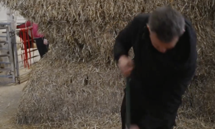 Person working with hay bales in a barn.