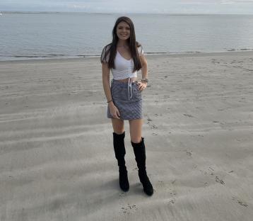 Woman in a white top and gingham skirt standing on a beach.