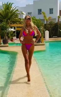 Woman in purple and orange bikini walking by a pool.