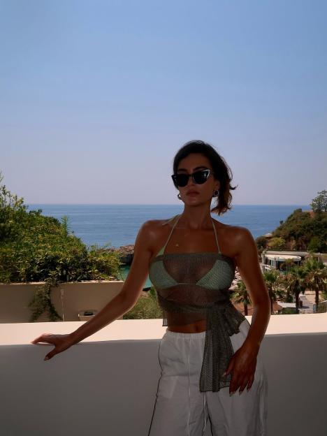 Woman in sunglasses on balcony overlooking ocean.