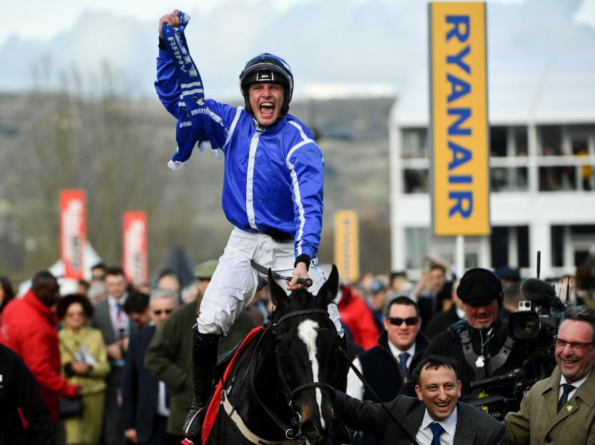 Jockey Paul Townend celebrates his victory at the Cheltenham Racing Festival, raising his right arm with a scarf.