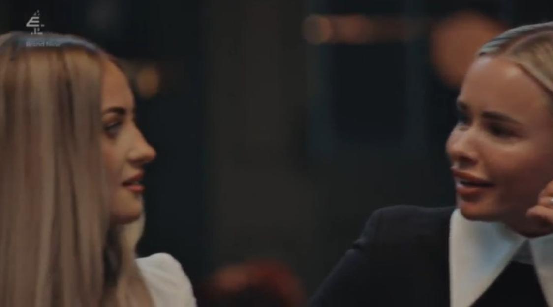 Two women looking at each other, one on the right smiling slightly and one on the left with a neutral expression.