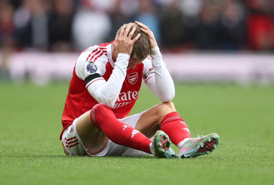 Arsenal's Martin Ødegaard sitting on the grass holding his head, with hands on his hair, after sustaining an injury.