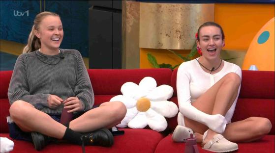 Two women laughing on a red couch.