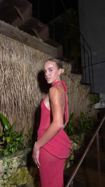 A woman in a red halter-neck dress looks over her shoulder at the camera.