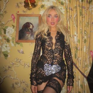 Sabrina Carpenter in a black lace dress, posing against a floral wallpaper.