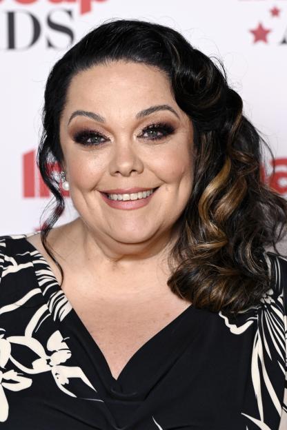 Lisa Riley smiles while wearing a black dress with white patterns.