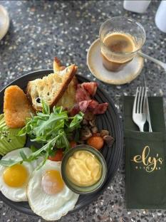 A plate of breakfast food with eggs, bacon, toast, and avocado, served with a cup of coffee.