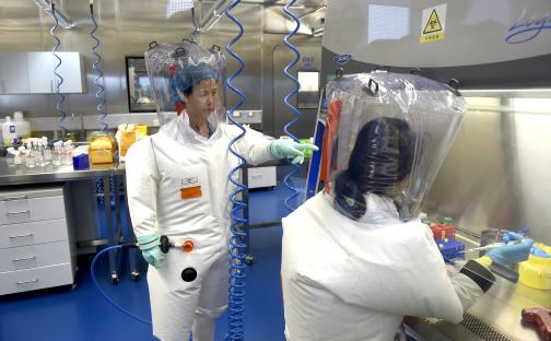 Two scientists in protective suits work in a lab.