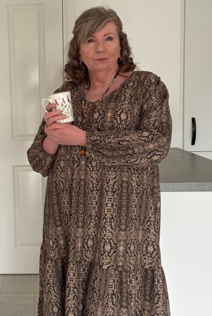 Lesley Thomas in a brown patterned dress, holding a mug.