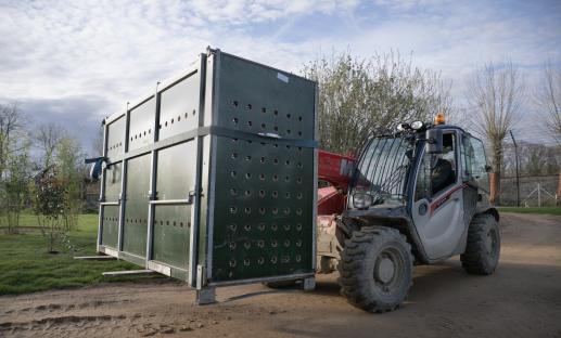 Forklift moving a large crate with holes.
