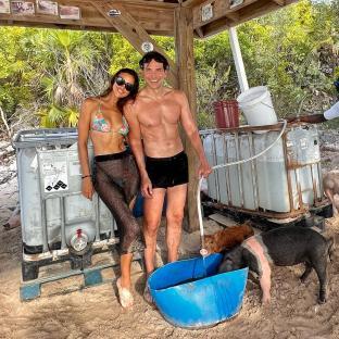 Irina Shayk and Bradley Cooper with pigs on a beach.