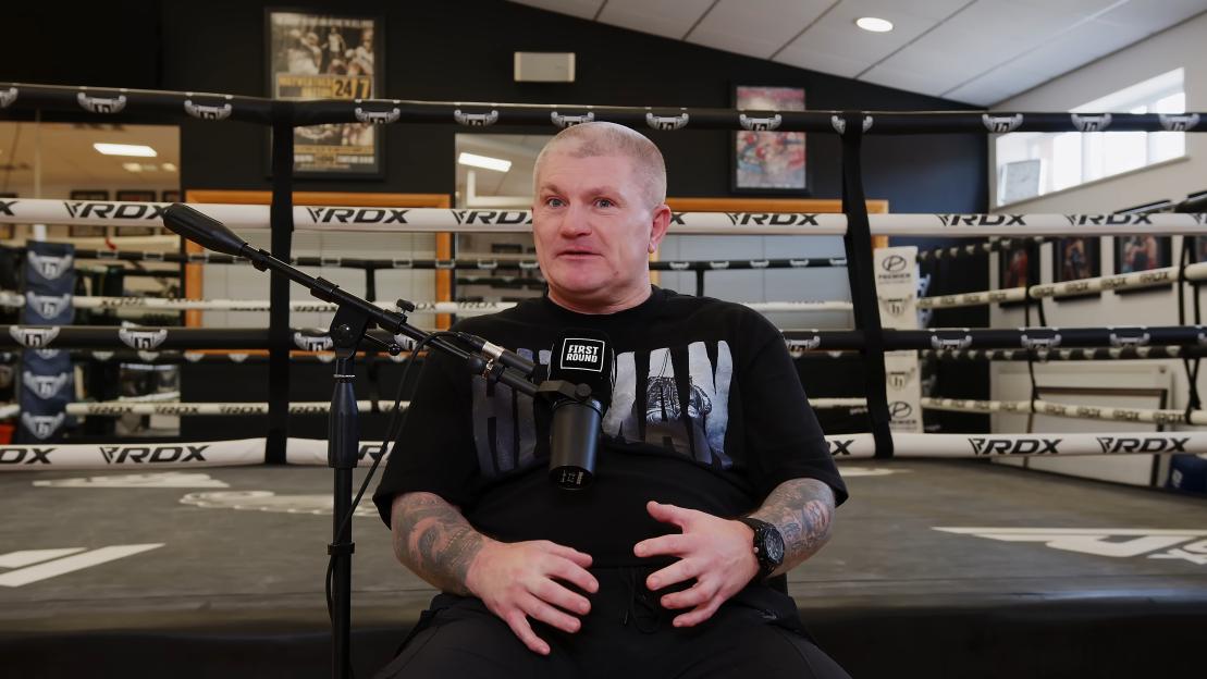 Ricky Hatton speaking into a microphone, sitting by a boxing ring.