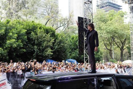 Tom Cruise waving to fans from a car at a Mission: Impossible premiere.