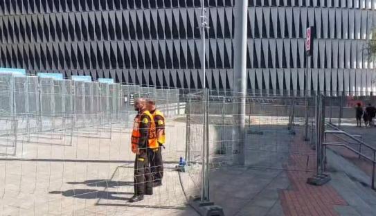 Two security guards standing behind a fence in front of a building.