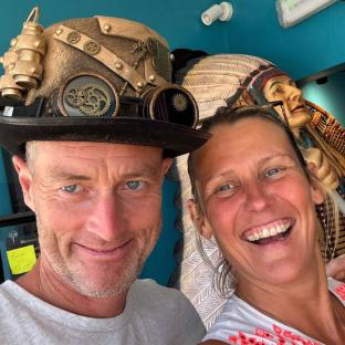 Close-up selfie of a man and woman; the man is wearing a steampunk-style hat.