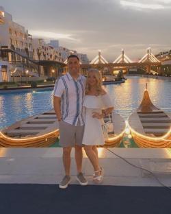 Couple posing by illuminated boats at a resort.