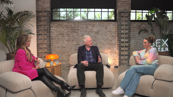 Three people sitting on beige couches and talking.