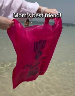 Person holding a pink plastic bag in shallow water.