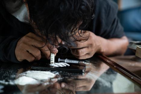 Person using a rolled-up bill to snort drugs from a smartphone screen.