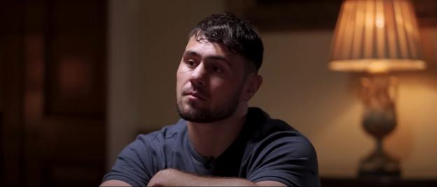 Man in a dark shirt sits and looks thoughtfully to the side.