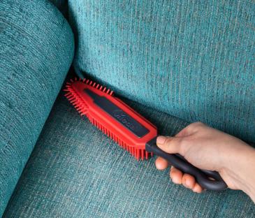 Hand using a red electrostatic brush to clean a teal fabric couch.