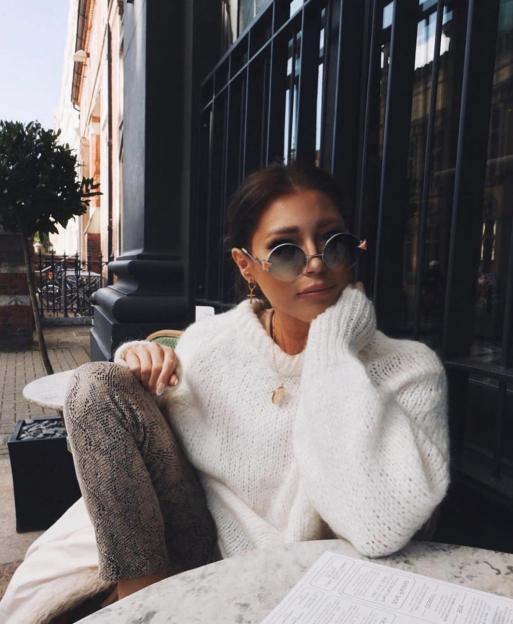 Woman in white sweater and sunglasses sitting at an outdoor table.