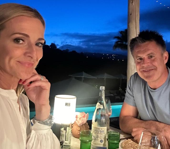 Gabby Logan and her husband looking at the camera during a nighttime dinner.