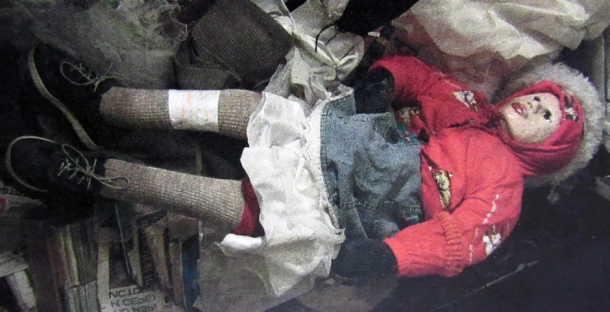 A child's body lying amidst discarded clothing and debris.