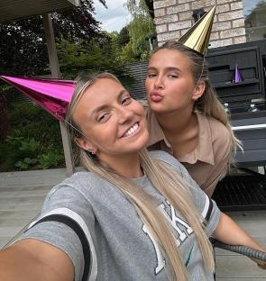 Two blonde women wearing party hats take a selfie.