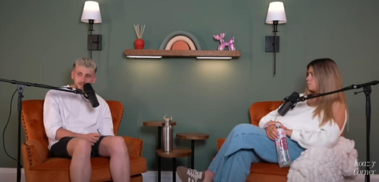A man and woman sitting in orange chairs during a podcast interview.