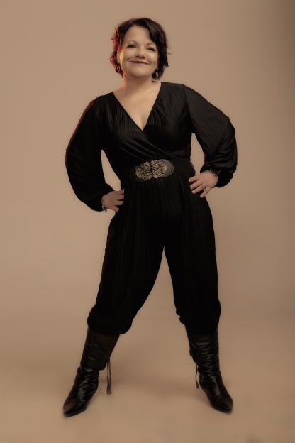 Woman in black jumpsuit and boots, smiling.