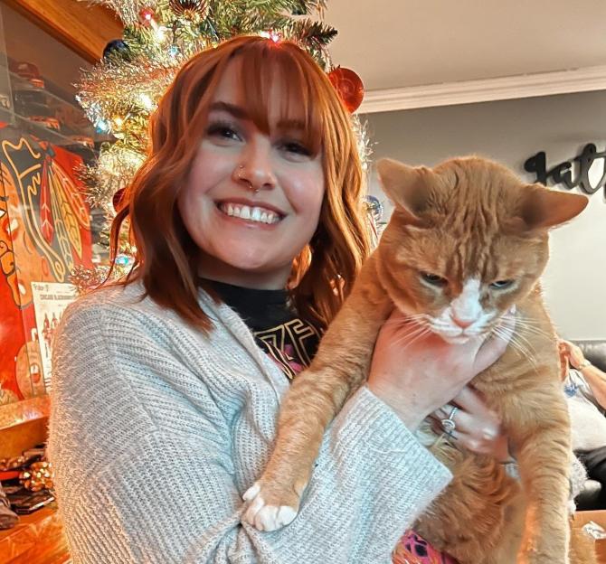 Woman holding an orange cat near a Christmas tree.