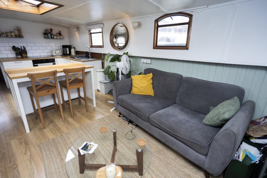 Interior of a houseboat showing a living area with a sofa and a kitchen area.