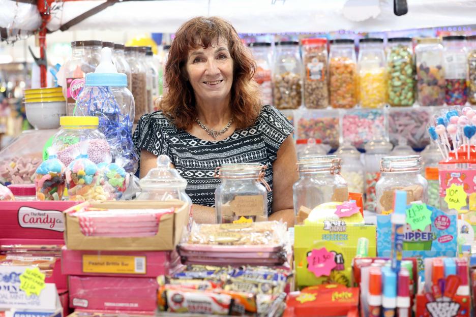 A woman smiles behind a counter full of jars and boxes of candy.