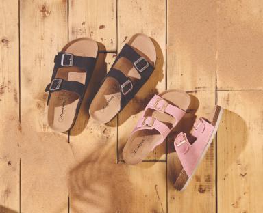 Two pairs of sandals on a wooden surface with sand.