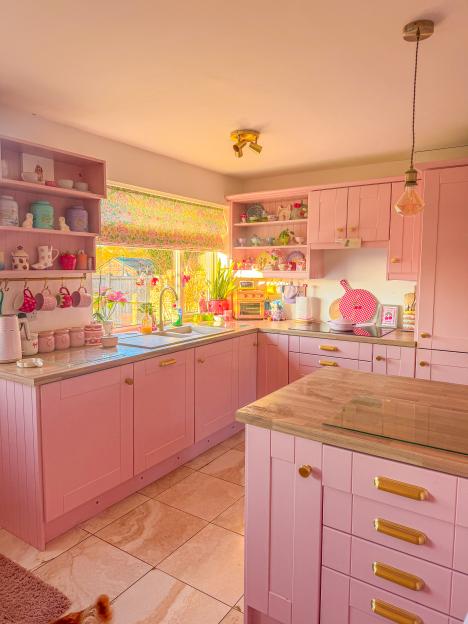 Pink kitchen with wood countertops and gold hardware.