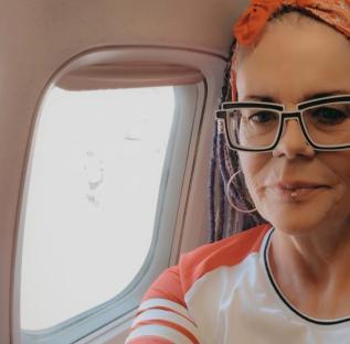 Woman on airplane wearing large glasses and red headband.