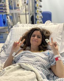 Woman in hospital bed giving peace sign.