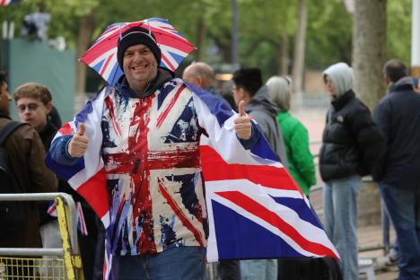 Man wearing Union Jack-themed clothing and umbrella gives thumbs up.