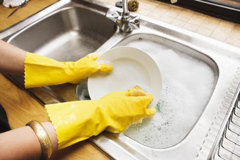 Person wearing yellow rubber gloves washing dishes in a kitchen sink.