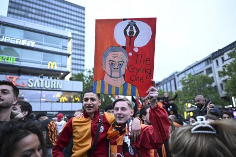 Galatasaray fans celebrating their Turkish Super Lig title victory, holding a sign depicting a crying man and a person holding a trophy.