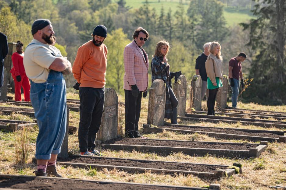 Contestants of a reality show standing next to their tombstones.