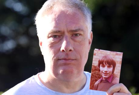 A man holds a photograph of himself as a child.