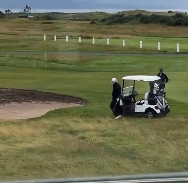 Golf caddy dropping a golf ball near a sand trap.