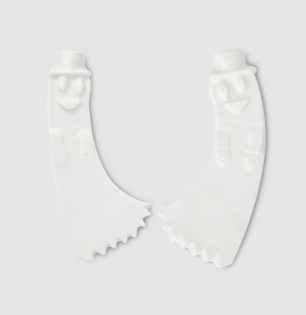 Two white, banana-shaped ceramic pieces with faces, one with a hat, and serrated edges.